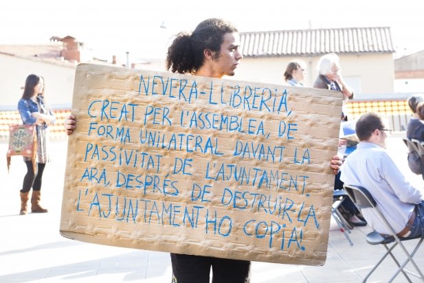Un jove de l'Assemblea Llibertària exhibeix un dels cartells de protesta durant l'acte
