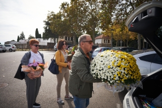 Una família amb diversos rams i centres de flors al pàrquing del cementiri el dia de Tots Sants de l'any passat